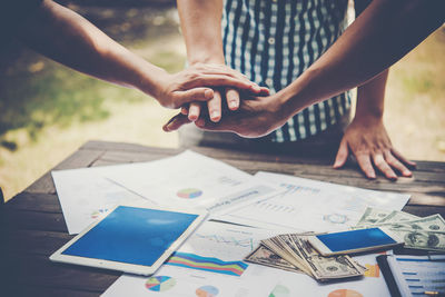 Midsection of colleagues stacking hands by charts and paper currency on table