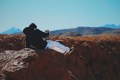 Man sitting on rock against sky