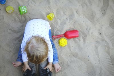 High angle view of playful girl with shoes and toys at sandy beach