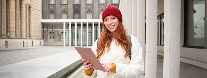 Portrait of young woman standing against building