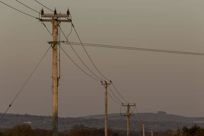 Low angle view of electricity pylon against sky during sunset