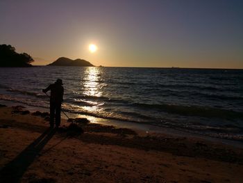 Silhouette people on beach against sky during sunset