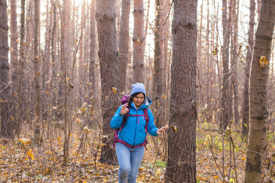 Full length of girl standing by tree trunk in forest