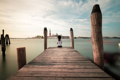 Rear view of woman sitting by grand canal on pier