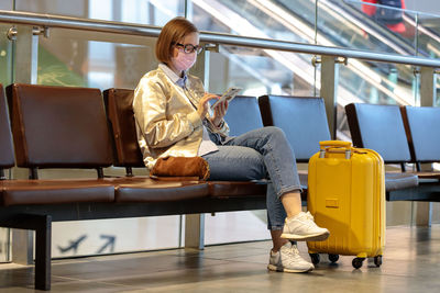 Woman using mobile phone while sitting by suitcaase at airport