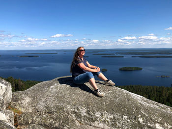 Young woman sitting on rock by sea against sky