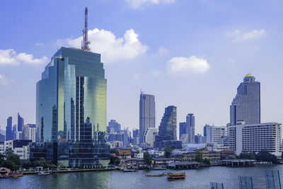 Modern buildings by river against sky in city