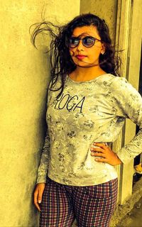 Young woman wearing sunglasses standing against yellow wall