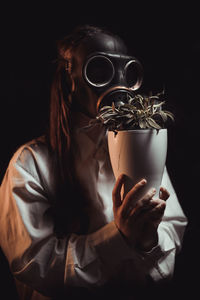 Close-up of woman wearing mask against black background