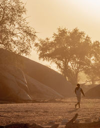 Side view of man standing on land against sky during sunset