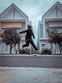 Man jumping by building against sky