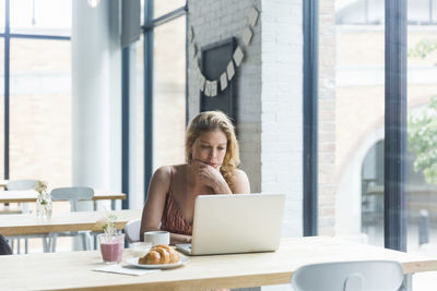 Woman with hand on chin using laptop computer while sitting in cafe