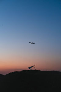 Silhouette airplane flying against clear sky during sunset