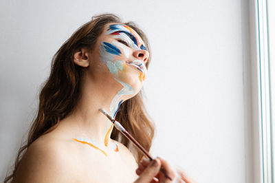 Close-up of young woman applying face paint against wall