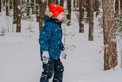 A boy walks in the snow in the winter forest. a child throws snow over his head.