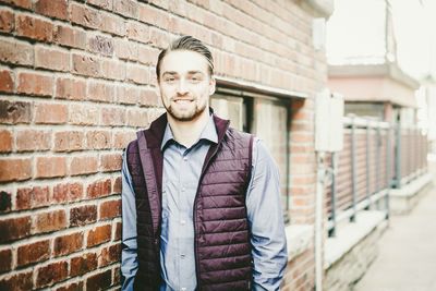 Portrait of smiling young man standing by brick wall