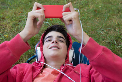 Top view portrait of young man with mobile phone and headphones lying in the field