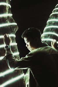 Side view of young man looking at illuminated lamp