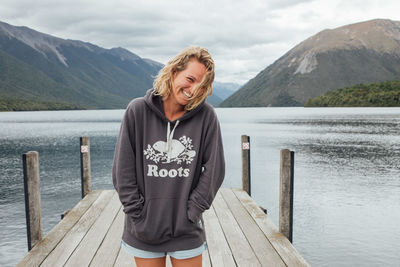 Portrait of smiling young woman standing on pier against lake