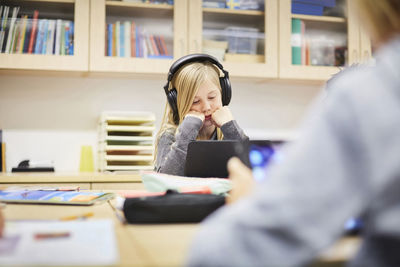 Girl wearing headphones while looking at digital tablet at desk in classroom