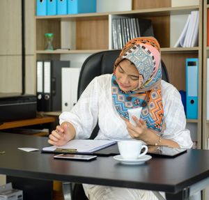 Midsection of woman holding coffee while sitting at table at home