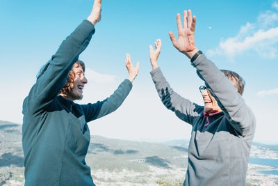 Smiling females with arms raised against sky