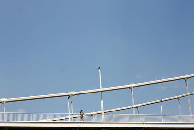 Man walking on bridge against blue sky