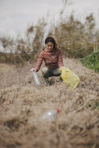 Woman crouching and collecting plastic bottles at countryside