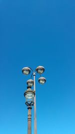 Low angle view of lamp posts against clear blue sky