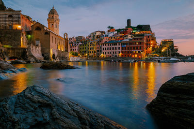 Illuminated buildings by river against sky