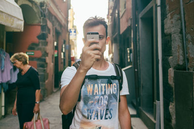 Young man on narrow street photographing with smart phone