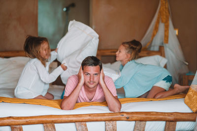 Portrait of father lying down on bed while daughters playing in background