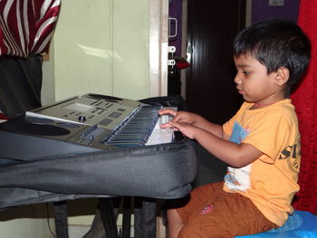 Side view of boy playing piano while sitting at home