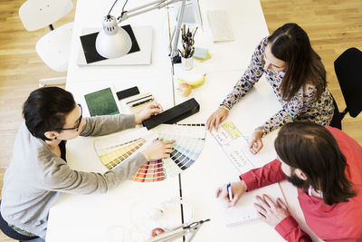 High angle view of business people discussing over color swatches at desk in office