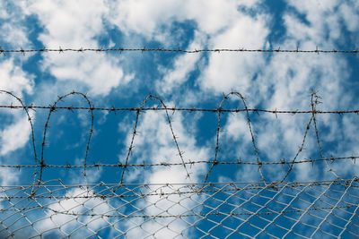 Low angle view of barbed wire fence against sky