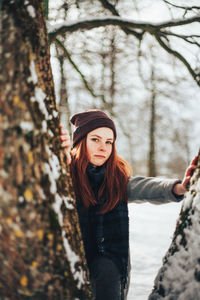 Smiling young woman standing by trees during winter