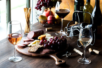A dark rustic scene of wine and cheese against a bright window.