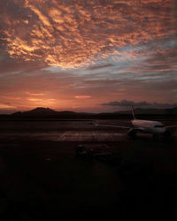 Airplane on runway against sky during sunset