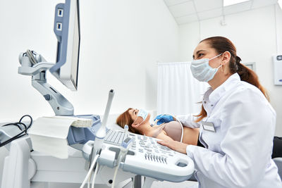 Side view of doctor wearing mask examining patient at clinic