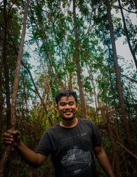 Portrait of young man standing against trees in forest