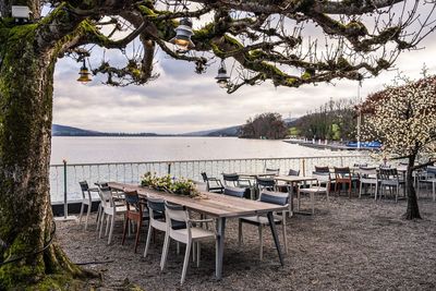 Empty chairs and tables at beach against sky