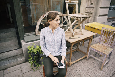 High angle view of woman with smart phone sitting on chair against store