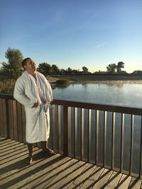 Man standing on railing by lake against sky