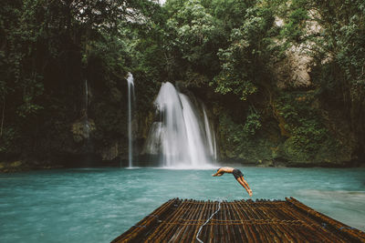 Shirtless man diving into lake from floating platform at forest