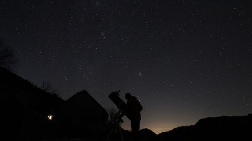Silhouette man with telescope on field against star field