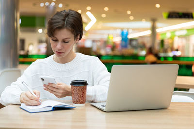 Portrait of young woman using mobile phone at table