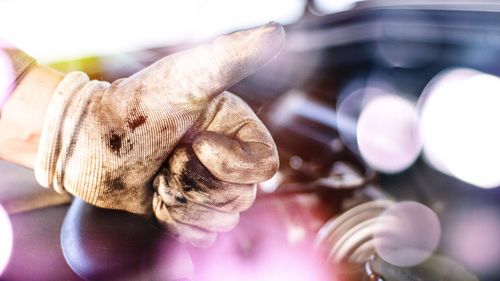 Cropped hand of mechanic gesturing thumbs up sign by car engine