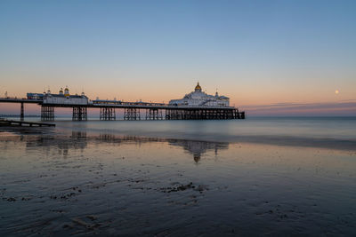 Wide view of eastbourne pier at sunset with moon in a clear sky