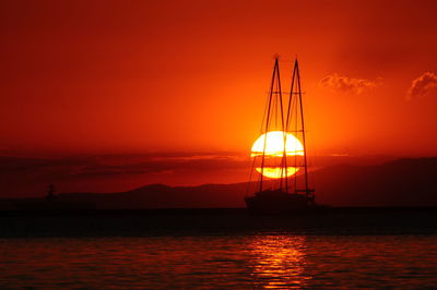 Silhouette sailboat on sea against orange sky