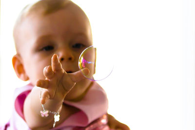 Baby girl reaching towards bubble against white background